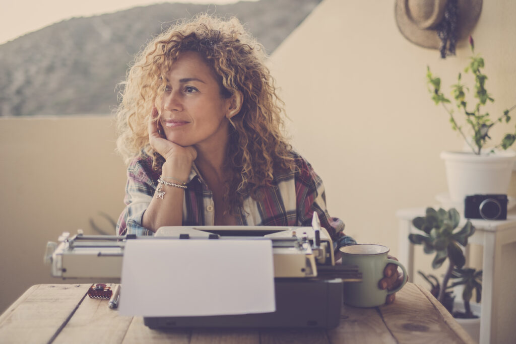 beautiful happy relaxed middle age caucasian woman blonde curly hair taking a break and stop writing with her old typewriter - blogger writer work and hobby time for hipster cheerful modern woman