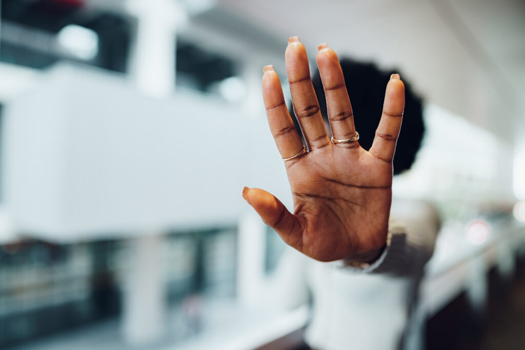 Portrait of a serious young african woman showing stop gesture with her palm in urban background, close up